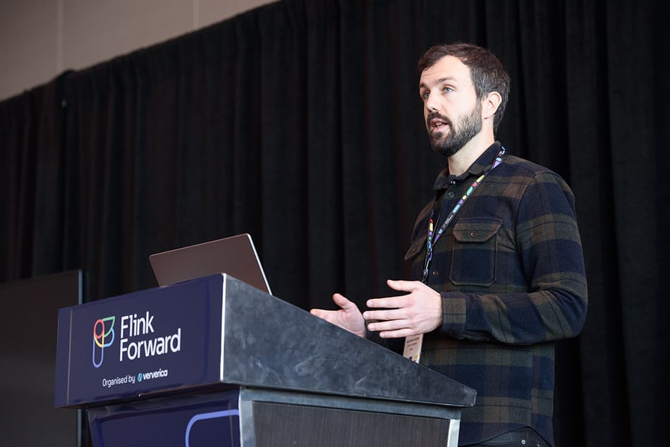 Presenter on the Flink Forward breakout stage, standing and speaking at the podium.